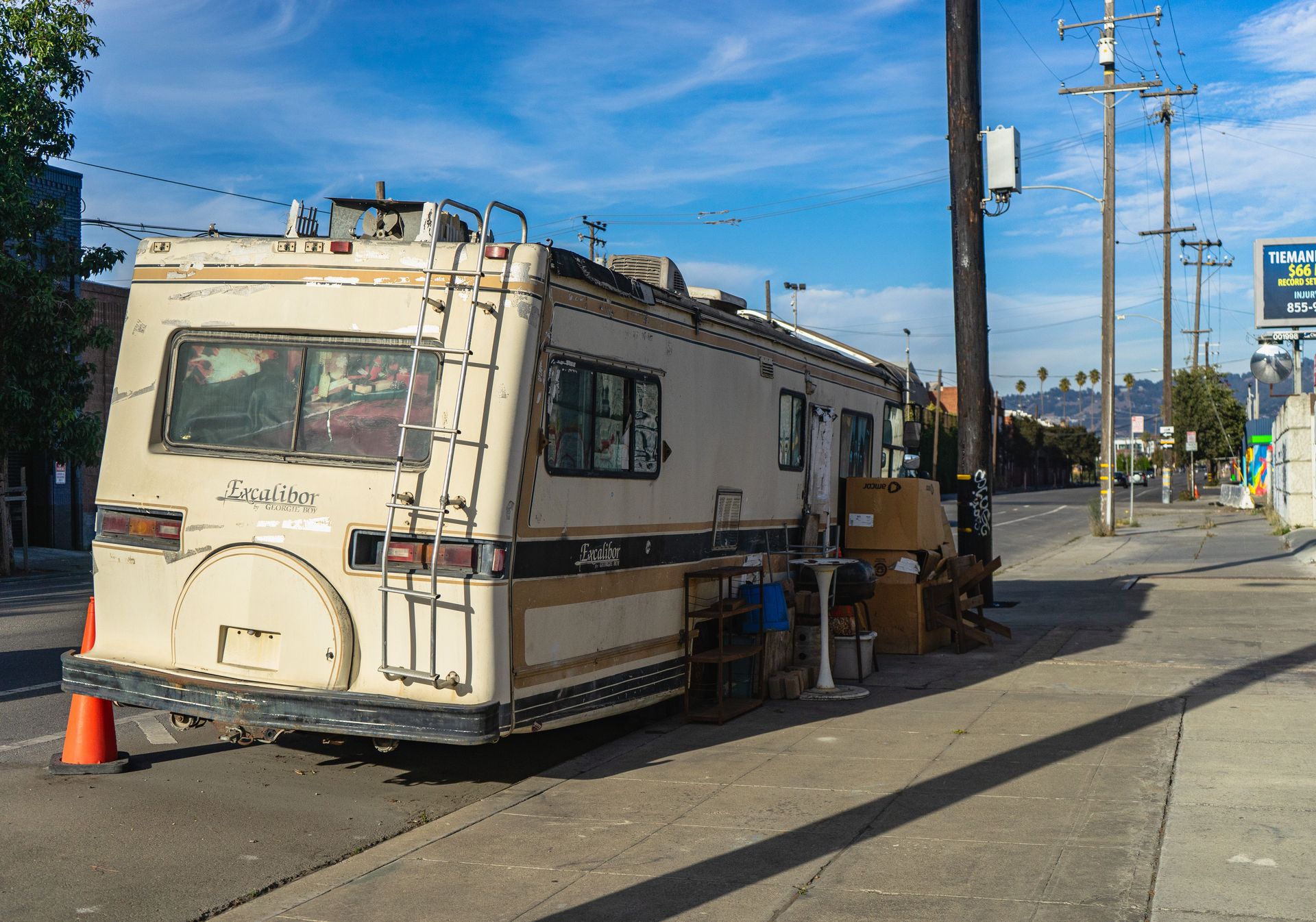 A vintage Excalibur RV parked on an urban street with scattered items outside.